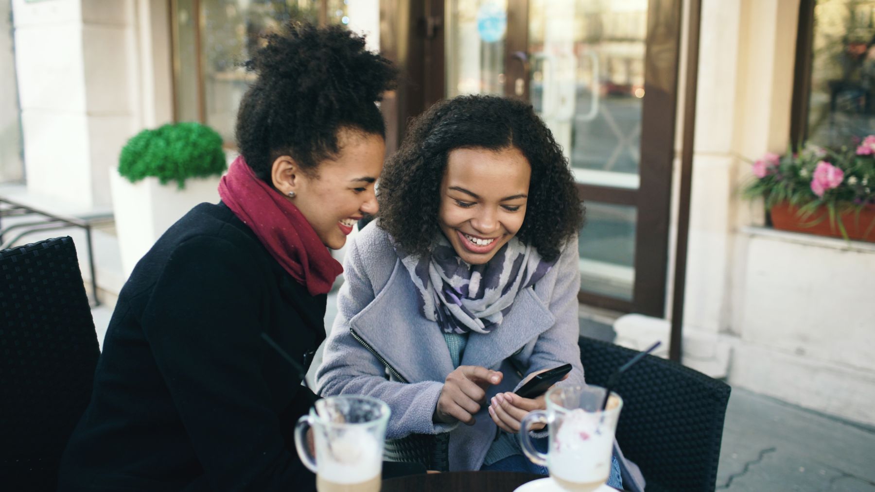 Two friends sharing something on a phone over coffee